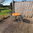 Moderne ronde cafétafel voor buiten met houten blad en groene designstoelen op een ruim houten terras.
