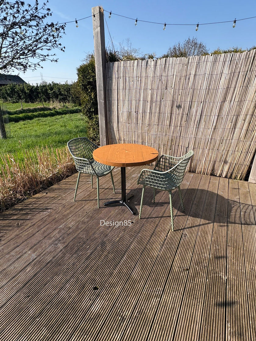 Moderne ronde cafétafel voor buiten met houten blad en groene designstoelen op een ruim houten terras.