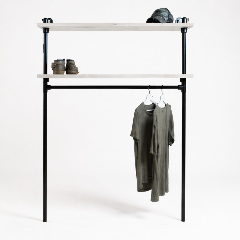Industriële kledingkast van zwart staal met twee legplanken van vurenhout in witte wax, op een witte achtergrond met hangende T-shirts, boots en pet.
