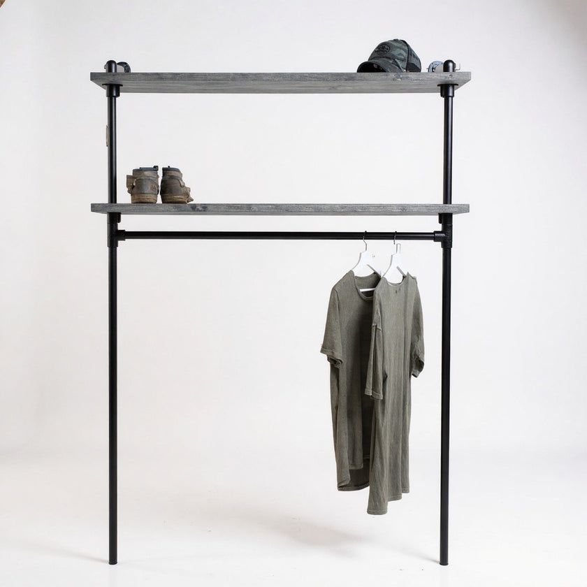 Industriële kledingkast van zwart staal met twee legplanken van vurenhout in zwarte wax, op een witte achtergrond met hangende T-shirts, boots en pet.