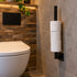 Industriële WC rolhouder Vierkant van zwart staal met drie toiletrollen, aan de muur gemonteerd naast een modern wit toilet in een sfeervolle industriële toiletruimte.