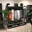 Industrieel kledingrek wielen Garderobe in een kledingwinkel, gevuld met dameskleding en voorzien van ruimte voor schoenen en tassen.