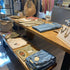 Grote presentatietafel winkel van Design85 met kleding, sieraden en tassen op twee houten niveaus.