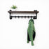 Steigerbuis kapstok met zwarte steigerbuizen en eiken legplank in black kleur, met groene jas en plant op witte achtergrond.