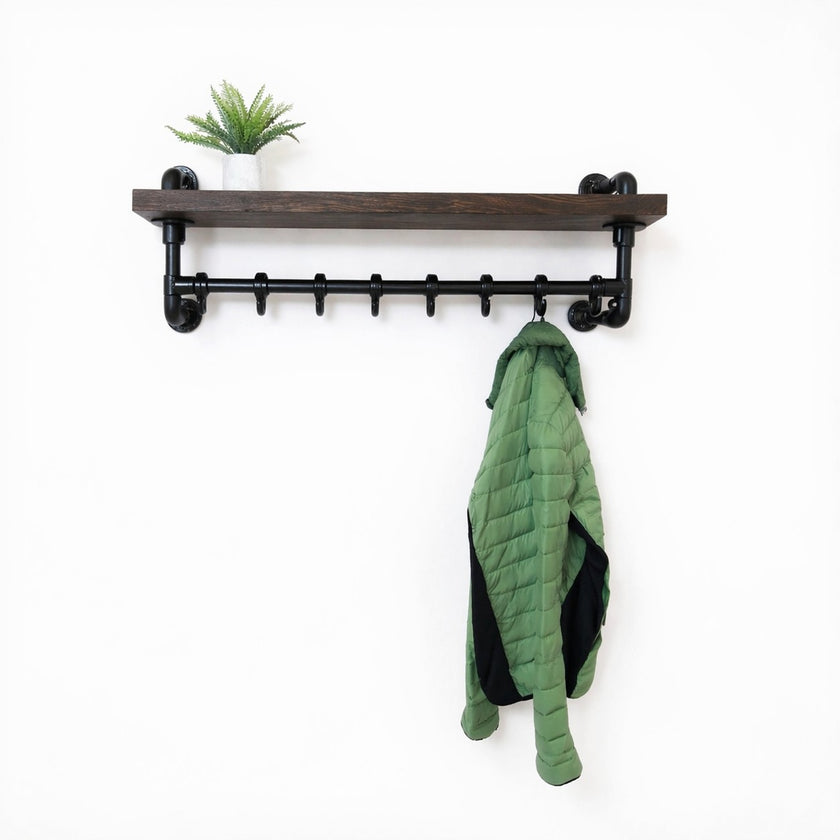 Steigerbuis kapstok met zwarte steigerbuizen en eiken legplank in black kleur, met groene jas en plant op witte achtergrond.