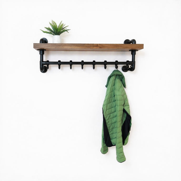 Steigerbuis kapstok met zwarte steigerbuizen en eiken legplank in sand kleur, met groene jas en plant op witte achtergrond.