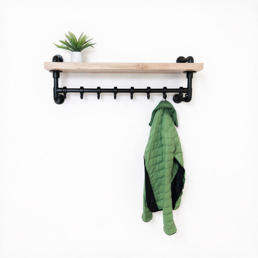 Steigerbuis kapstok met zwarte steigerbuizen en eiken legplank in white kleur, met groene jas en plant op witte achtergrond.